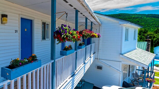 A white building with a blue door and windows, a covered porch with blue railings, and hanging flower baskets. - Parkers Motel (Lincoln)