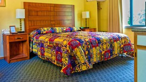 A hotel room with a wooden headboard, a colorful quilted bedspread, two bedside lamps, a desk with a telephone, and a window with curtains. - Parkers Motel (Lincoln)