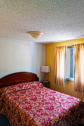 A bedroom with a floral bedspread, a wooden headboard, a bedside lamp, and a window with curtains. - Parkers Motel (Lincoln)