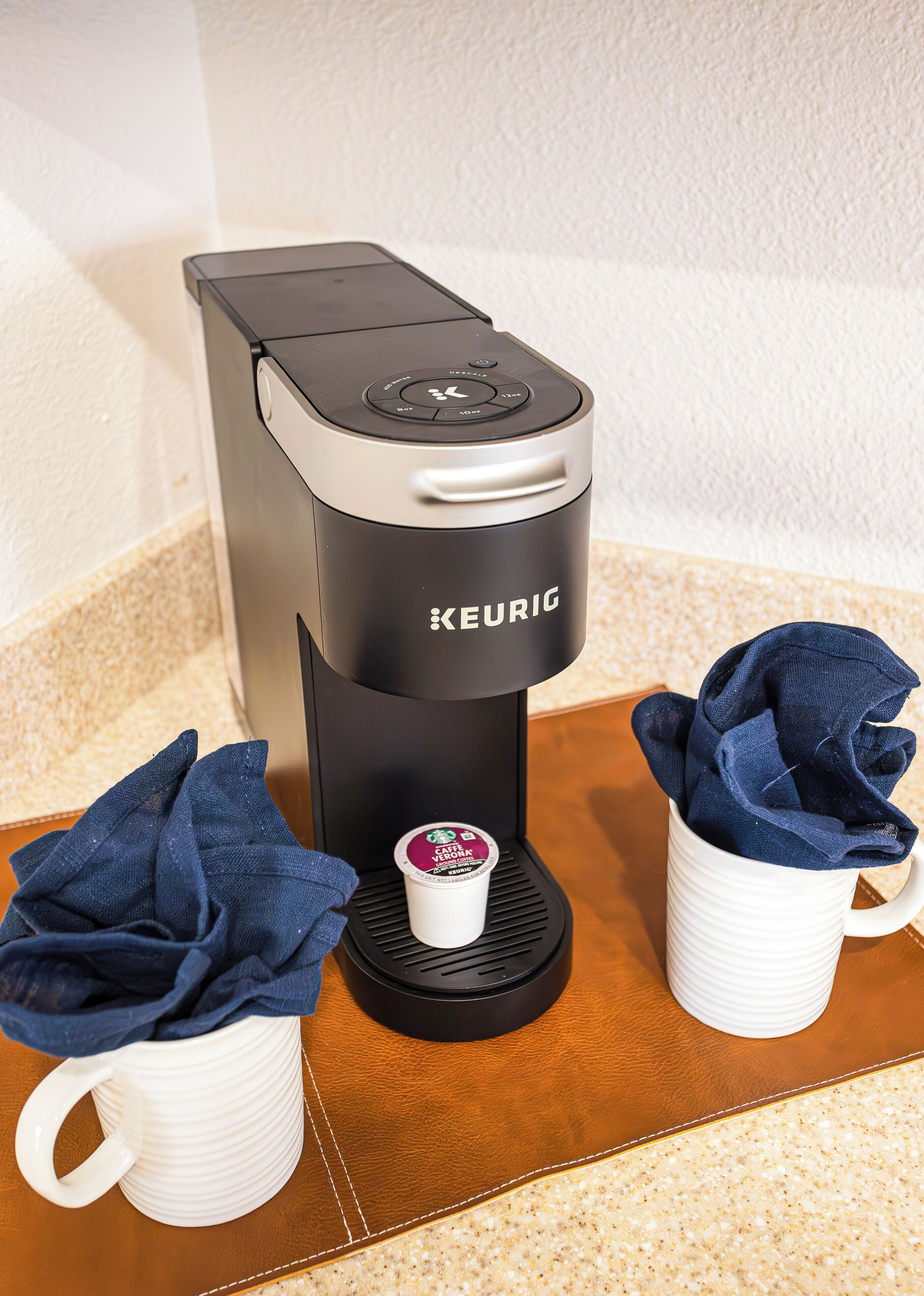 Eine Kaffeemaschine von Keurig mit zwei weißen Tassen und einer Stoffserviete auf einem Holztisch.