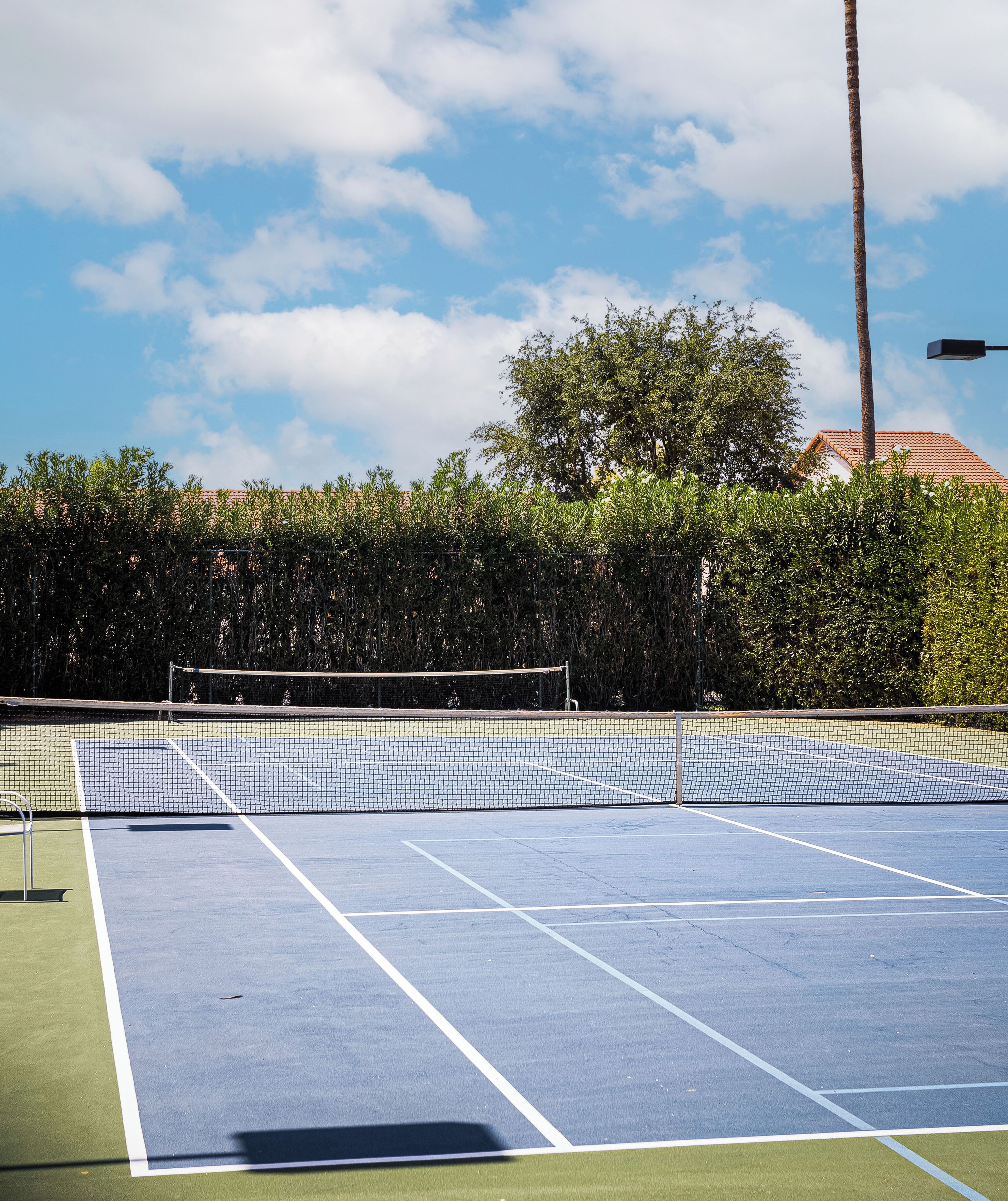 A tennis court with a net, surrounded by trees and a building with a red roof.
