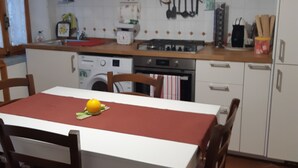 Une cuisine de taille modeste, avec des meubles blancs, une nappe rouge et un citron posé sur la table.