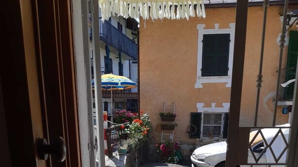 Une porte donnant sur une cour intérieure où l’on aperçoit une voiture blanche garée au fond, un petit jardin fleuri et un bâtiment doté d’un balcon.