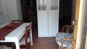 Un coin repas avec une table et des chaises blanches, un meuble avec des portes en verre et une chaise à motifs.