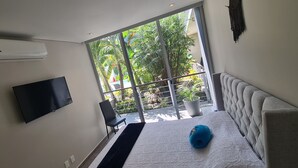 Ein modernes Wohnzimmer mit einem Flachbildfernseher, einem grauen Sofa und einem großen Fenster mit Blick auf Grün.