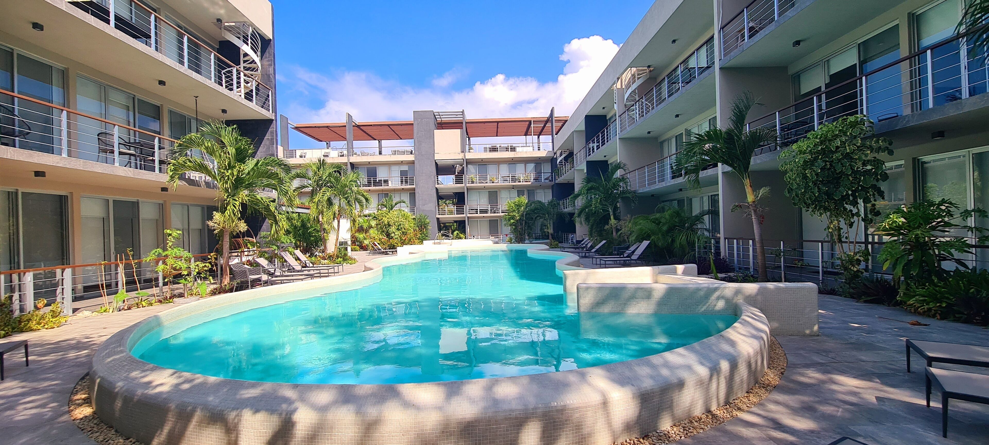 Un hôtel moderne doté d’une piscine centrale, entourée de chaises longues et de palmiers.
