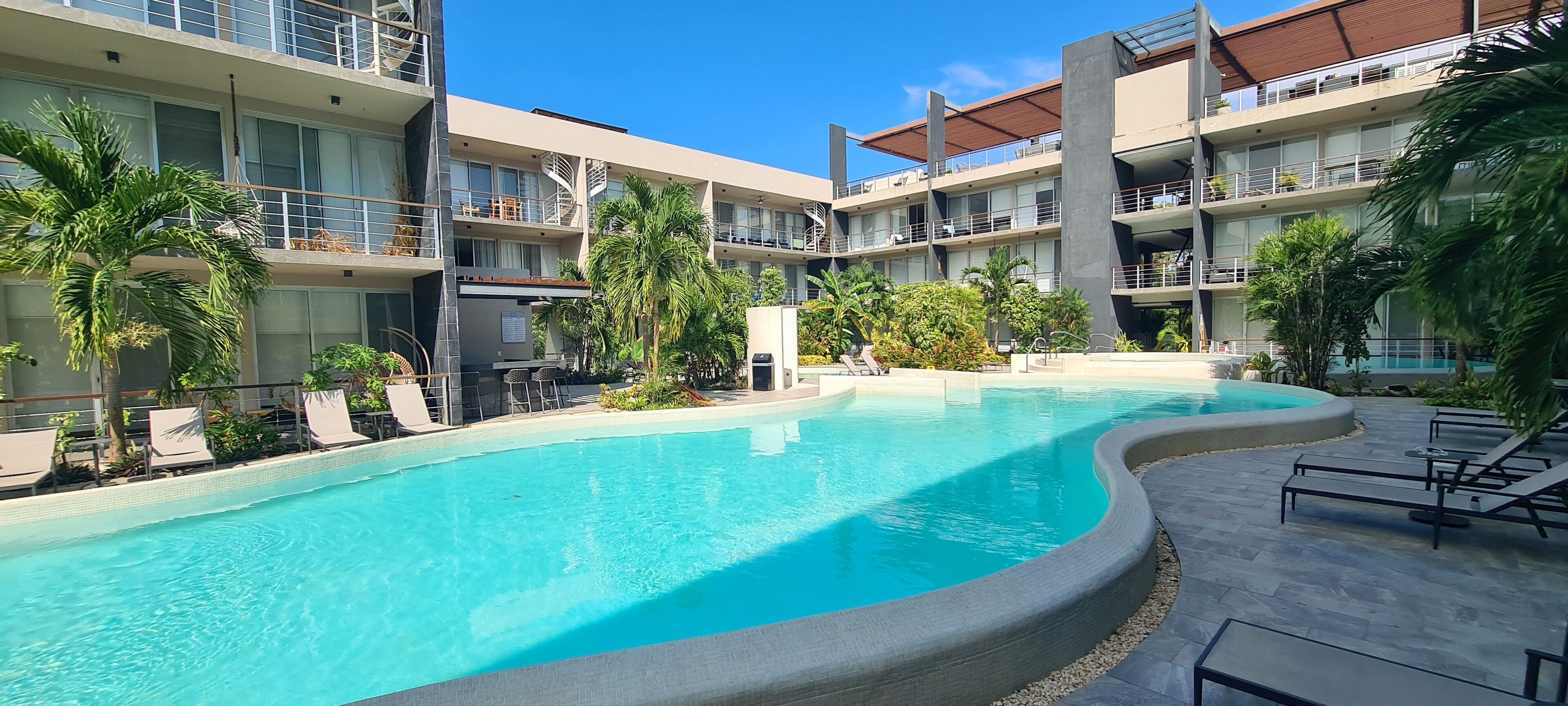 A hotel with a swimming pool, lounge chairs, and palm trees.