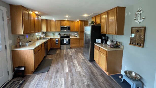 A kitchen with wooden cabinets, stainless steel appliances, and a small pet feeding station. - A W🌊VE From It All! Secure boat storage, huge yard, lots of outdoor games! (Page)