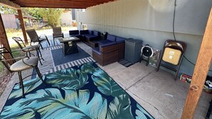 A covered patio area with seating, a table, and a trash can. - A W🌊VE From It All! Secure boat storage, huge yard, lots of outdoor games! (Page)