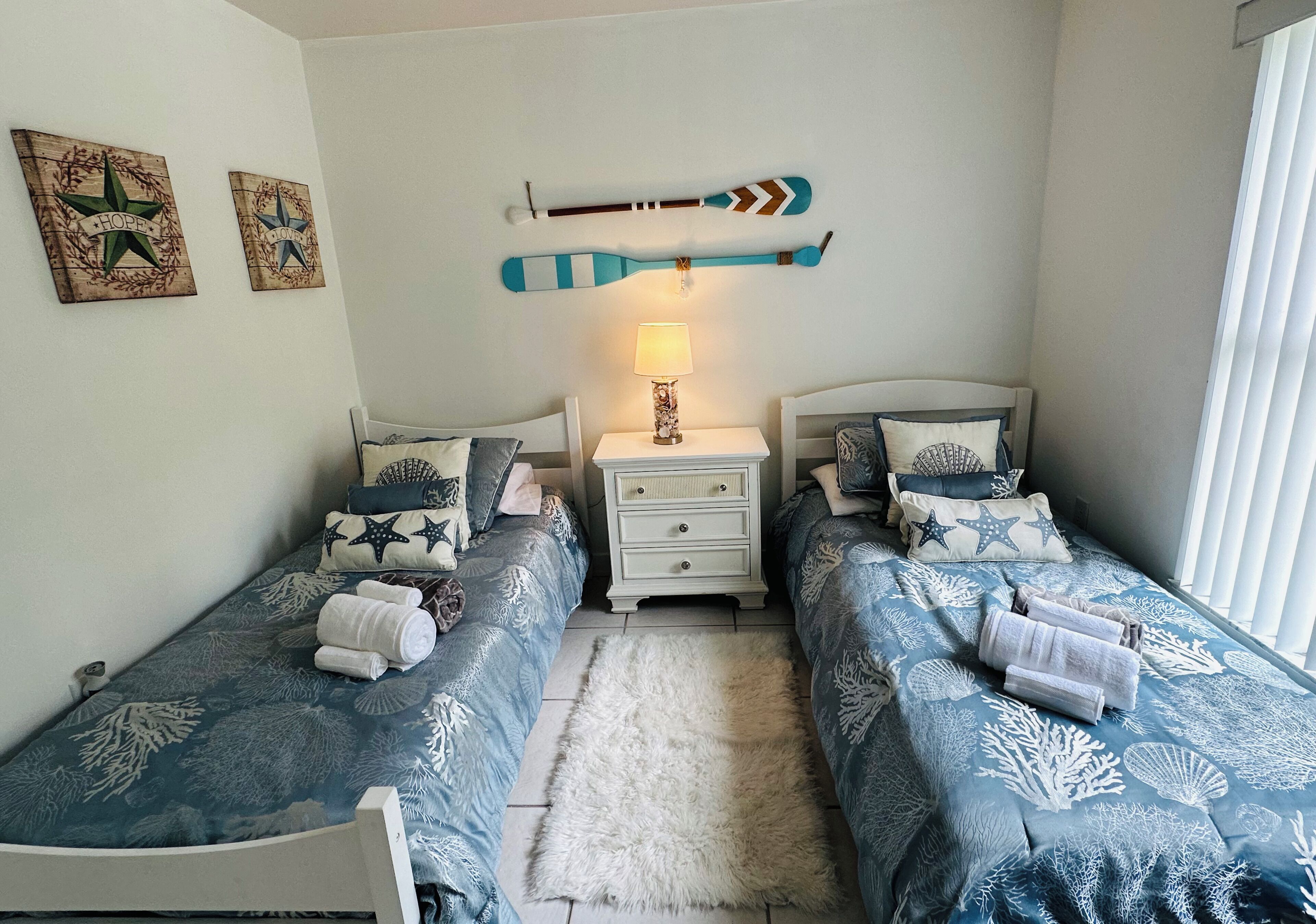 A bedroom with two beds, a nightstand, and wall decorations.