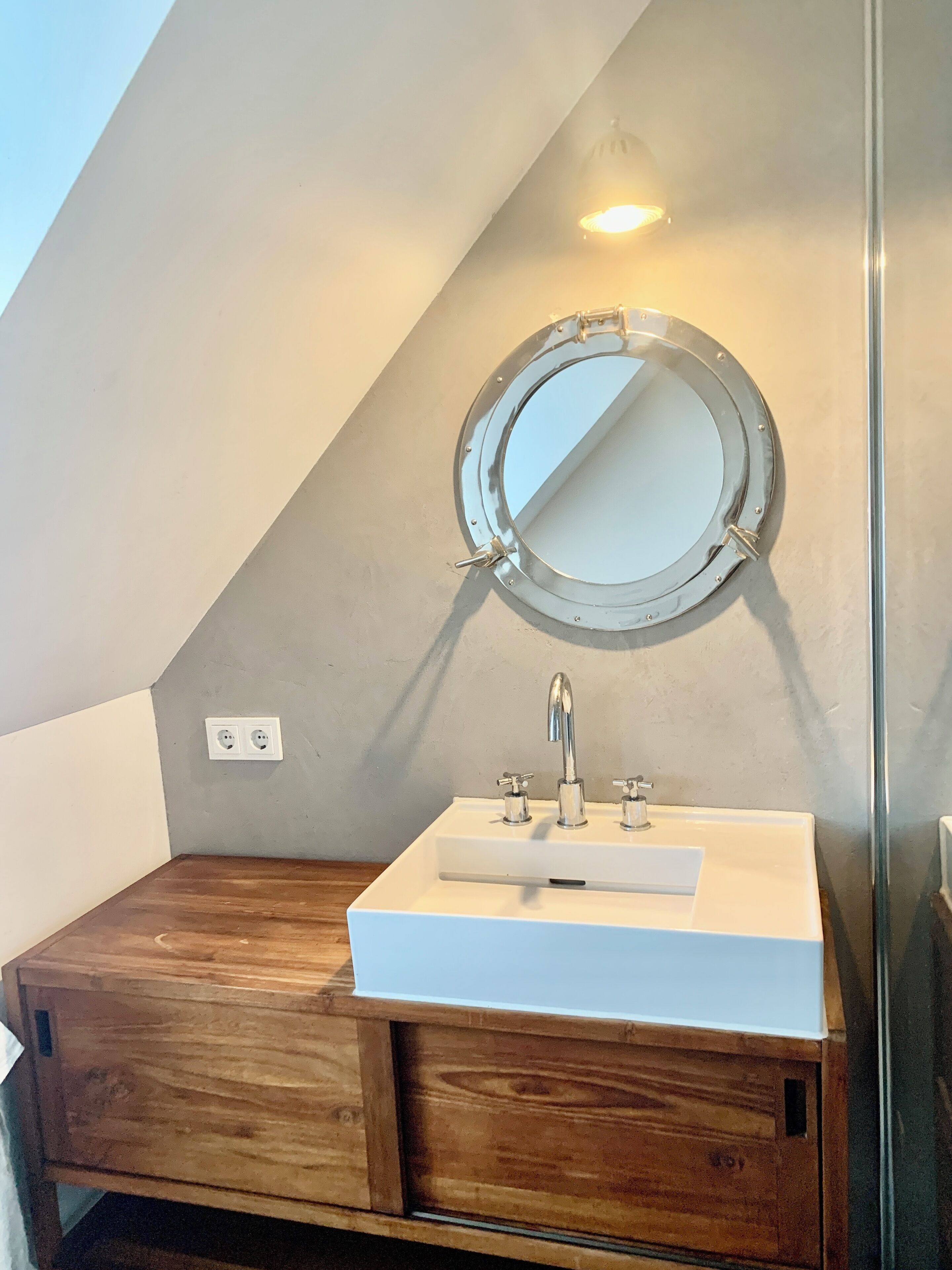 A bathroom with a white sink, a round mirror, and wooden cabinets.