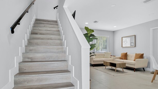 Eine Treppe mit Holzboden und weißen Wänden führt zu einem Wohnbereich mit Sofa und Couchtisch.