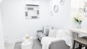 A modern, well-lit room with a grey sofa, a white coffee table, and a small white side table. There is a grey rug on the floor, and a white wall with a framed picture and a small air conditioning unit. - Oasis on Poitier in Nassau Bahamas - your private retreat. (Nassau)