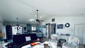 Amplia sala de estar con sofá, sillón y una mesa de centro. Se ve una cocina al fondo con una zona de comedor.