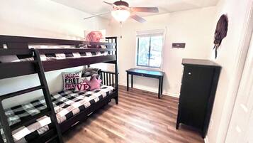 A room with bunk beds, a ceiling fan, a window, and a small table.