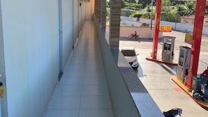 A corridor with air conditioning units, a tiled floor, and a gas station with fuel pumps and a motorcycle in the background. - Suite rooms in Pousada Jesus me Deu in Iguatu/Ce, 200m from the Airport. (Bugi Iguatu)