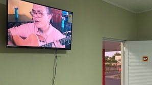 A television mounted on a wall displaying a person playing a guitar. - Suite rooms in Pousada Jesus me Deu in Iguatu/Ce, 200m from the Airport. (Bugi Iguatu)