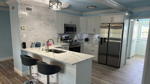 A modern kitchen with white cabinetry, a stainless steel refrigerator, and a marble countertop. - Island Cottage in Quaint Matlacha Florida. Amazing island life is a click away… (Matlacha)