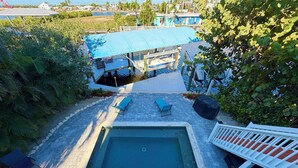 A swimming pool with a deck, surrounded by greenery and a covered area with chairs. - Island Cottage in Quaint Matlacha Florida. Amazing island life is a click away… (Matlacha)