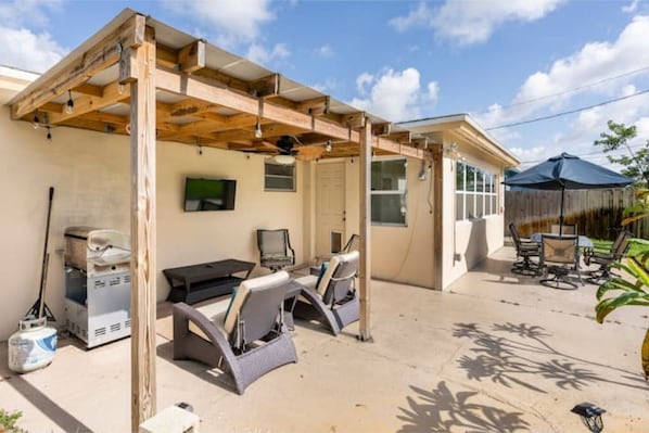 Un patio couvert comprenant un barbecue, des sièges et un téléviseur fixé au mur.