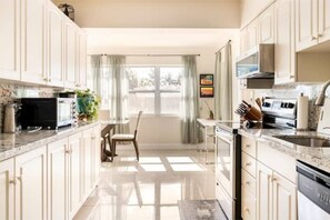 Une cuisine moderne avec des armoires blanches, un comptoir en marbre et une vue sur l’extérieur.