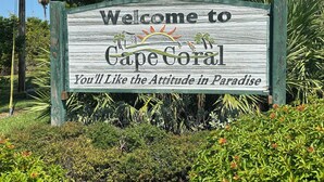 Un cartello di benvenuto per Cape Coral a tema tropicale, circondato da lussureggiante vegetazione.