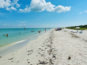 A beach with clear turquoise water, a sandy shore, and a pier in the distance.
