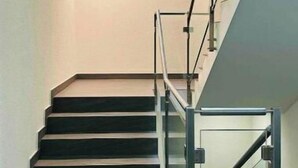 Un escalier moderne avec des rampes en verre et une main courante en métal, menant à l’étage supérieur.
