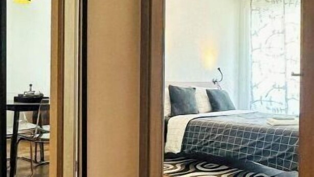 Une chambre d’hôtel avec un plancher en bois, un lit recouvert d’une courtepointe à motifs, un bureau avec une chaise et un luminaire suspendu.