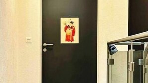 Un couloir avec une porte noire, un petit tableau encadré et une rambarde en verre.