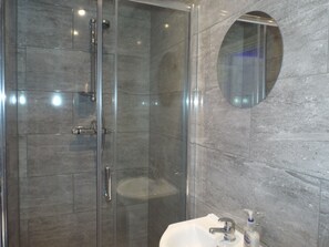 A modern bathroom with a glass-enclosed shower, a marble-tiled wall, and a round mirror.