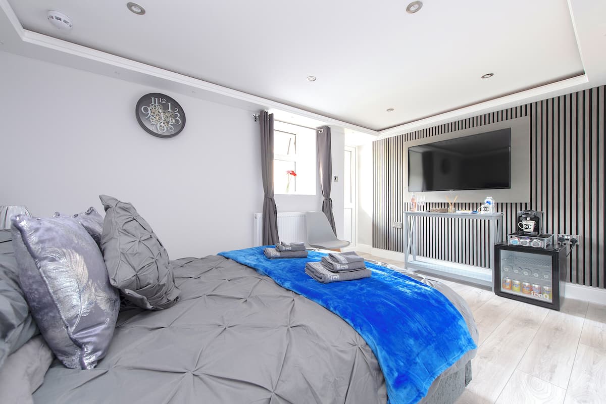 A modern bedroom with a large bed, a flat-screen TV mounted on the wall, and a small refrigerator with beverages.
