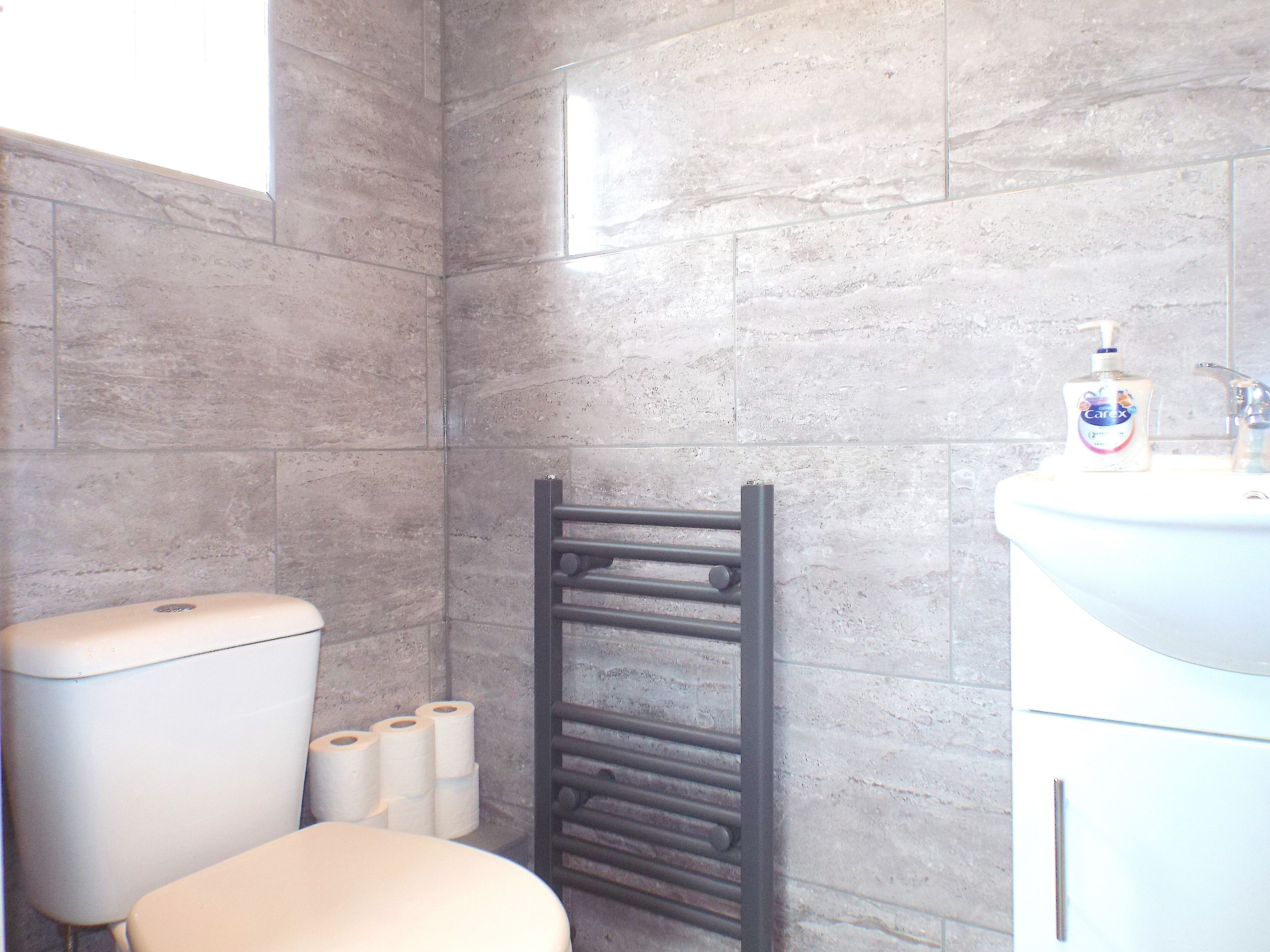 A bathroom with a toilet, a towel rack, and a sink with a bottle of hand soap.