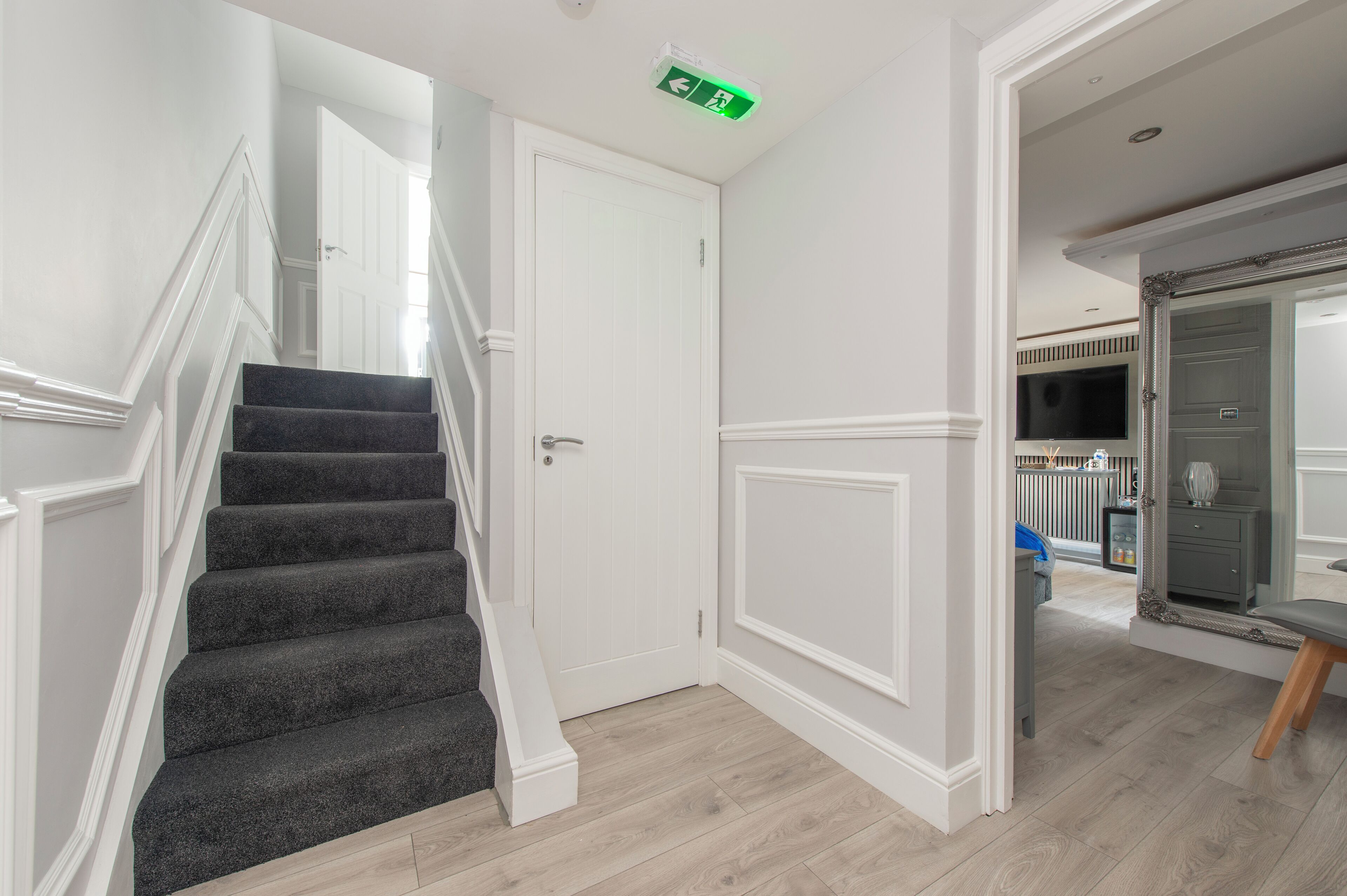 A staircase with a white door at the top leading to a room with a television and a mirror.