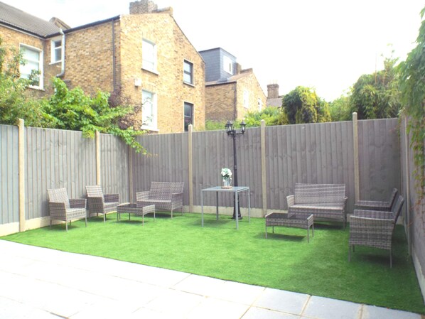 A backyard with a grassy lawn, wicker furniture, and a small table.