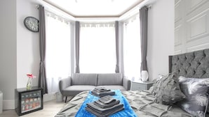 A bedroom with a bed, a bedside table, a nightstand, a window with curtains, and a wall clock. - The Pond House - Ensuite Rooms (London)