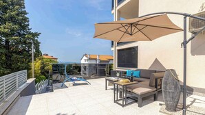 An outdoor patio with a sofa, table, and umbrella, overlooking a pool and buildings. - Holiday apartment with pool (Dramalj)
