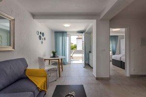 A modern living room with a sofa, a coffee table, and a dining area with a table and chairs. There is a doorway leading to a bedroom with a bed. - Holiday apartment with pool (Dramalj)