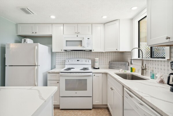 A modern kitchen with white cabinets, a built-in microwave, a stove, and a sink.