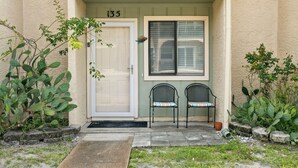Une entrée d’immeuble avec une porte portant le numéro « 135 », une fenêtre avec des stores et deux chaises à l’extérieur.