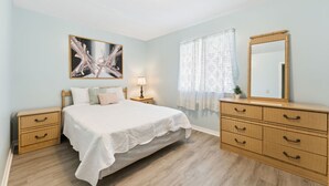Une chambre à coucher comprenant un lit, une table de chevet, une commode, un miroir, une lampe et un tableau accroché au mur.