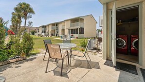 Une terrasse avec une table et des chaises, un lave-linge, et un immeuble avec de nombreux balcons en arrière-plan.