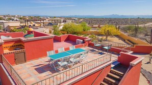 A rooftop patio with a table and chairs, surrounded by red walls and a view of a desert landscape.