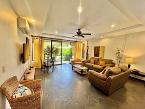 A spacious living area with a large sliding glass door leading to a patio, a ceiling fan, and a flat-screen TV mounted on the wall.