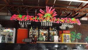 Zona de bar con un letrero de neón, taburetes y una variedad de botellas y vasos.