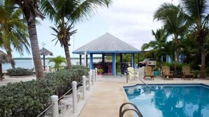 A pool area with a clear view of the water, a covered seating area, and palm trees. - Sunset Wishes on Bone Fish Flats (Hermitage)