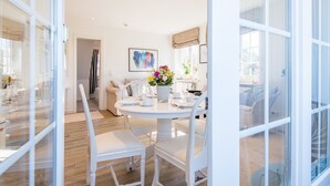 A bright, modern dining area with a round table, white chairs, and a vase of flowers. - Haus Skandia, App. 4 - Strandnahe 3-zimmer Ferienwohnung auf ca. 56 m² Wohnfläche, für bis zu 4 (Wenningstedt-Braderup (Sylt))