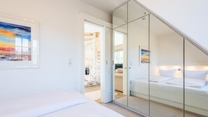 A bedroom with a bed, a glass partition, and a painting on the wall. - Haus Skandia, App. 4 - Strandnahe 3-zimmer Ferienwohnung auf ca. 56 m² Wohnfläche, für bis zu 4 (Wenningstedt-Braderup (Sylt))