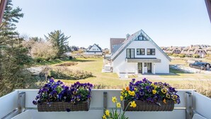 A modern house with a white exterior and a sloped roof, viewed from a balcony with flower baskets. - Haus Skandia, App. 4 - Strandnahe 3-zimmer Ferienwohnung auf ca. 56 m² Wohnfläche, für bis zu 4 (Wenningstedt-Braderup (Sylt))