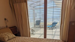 A hotel room with a large bed, a view of the pool area through the window, and a wooden dresser.
